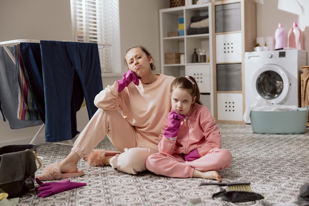 Housewife sitting on the floor with her daughter supporting herself under chin with a rubber glove resting women after work Exhausted girls tired after housework prepared for Christmas