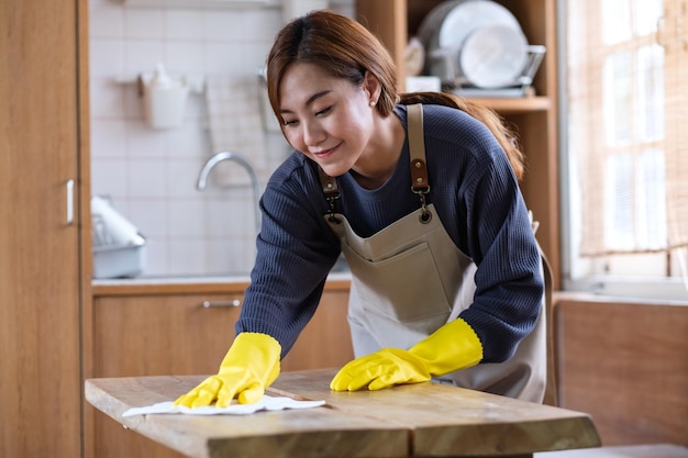 A housewife wearing protective glove cleaning and washing wooden table in the kitchen at home