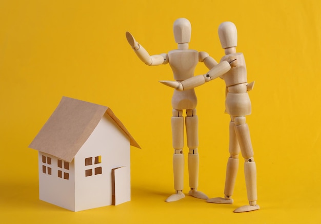 Housing sale concept Wooden puppets and house model on yellow background