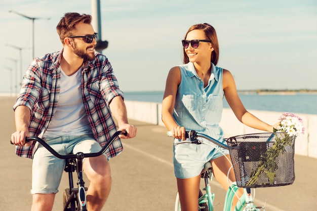 How about race? Cheerful young couple looking at each other with smiles while riding on bicycles along the road