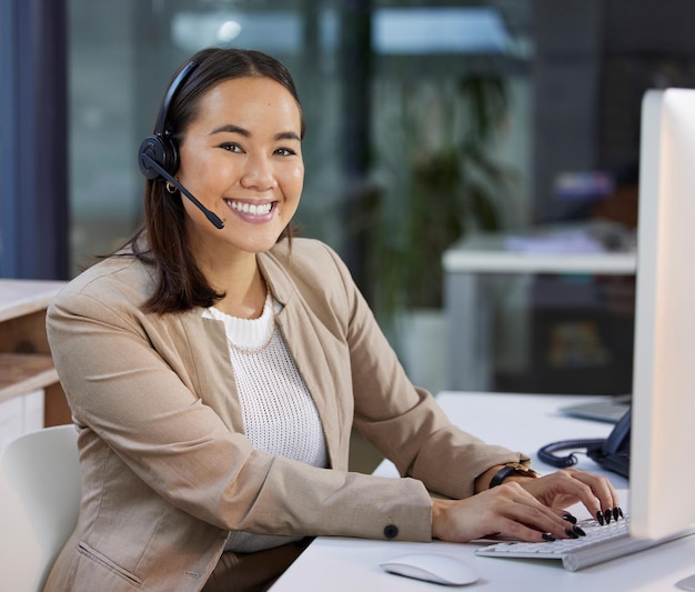 How can I make your experience a happy one Portrait of a young woman using a headset and computer in a modern office