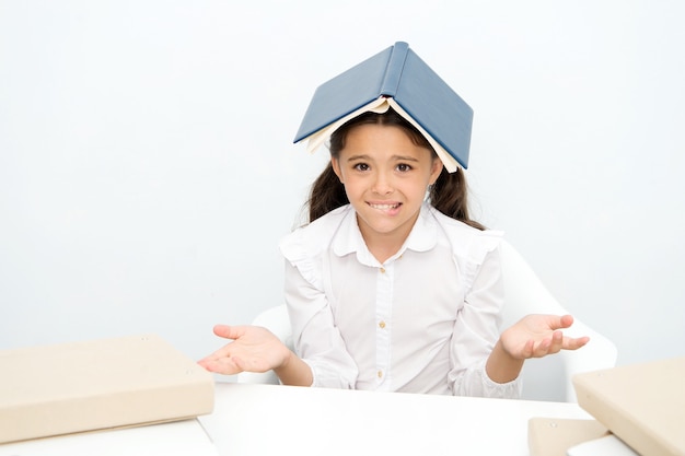 How is it possible to learn. Girl child confused exhausted with book roof on head white background. Schoolgirl tired of studying and reading. Kid school uniform tired face not want continue reading.