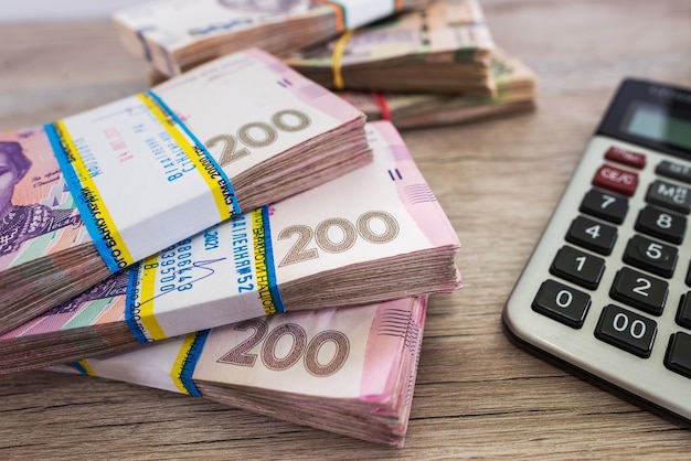 Hryvnia in bundles and a calculator on a wooden table.