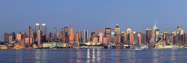 Hudson River waterfront view of New York City Manhattan after sunset with cityscape panorama and light reflection in tranquil blue tone.