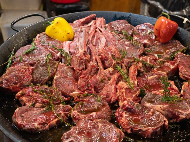 Huge pan with raw meat like ribs and steaks with spices and vegetables uncooked