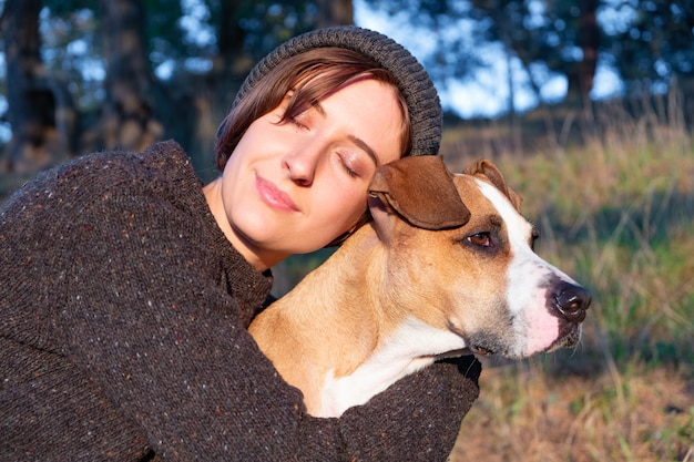 Hugging a dog in beautiful nature at sunset. Woman facing evening sun sits with her pet next to her