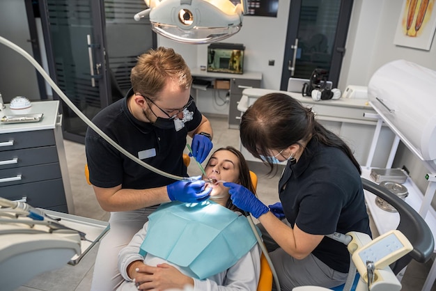 Human dentist is operating on a young smiling girl in a dental clinic