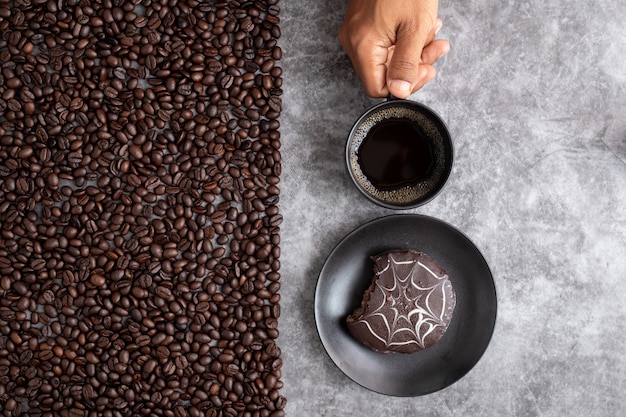 Human hand hold coffee mug and chocolate cake with coffee beans on cement texture background.