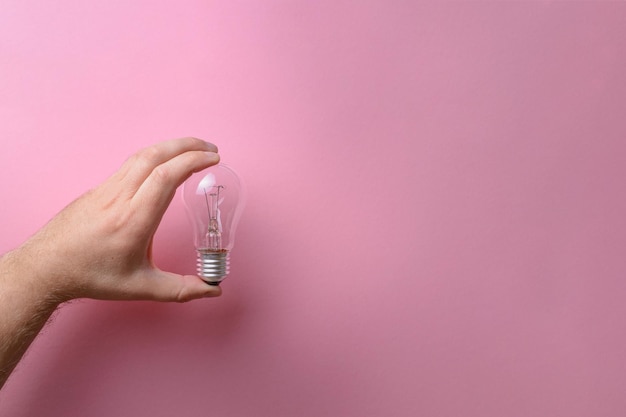 The human hand holds a glass light bulb on a pink background Creativity ideas inspiration concepts