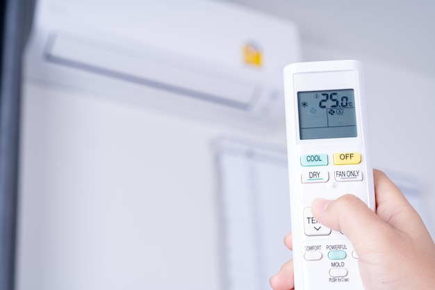 Human hand is using white remote of air conditioner