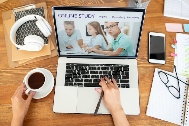 Human hand over laptop keypad surfing on website of distant learning while sitting by desk at home