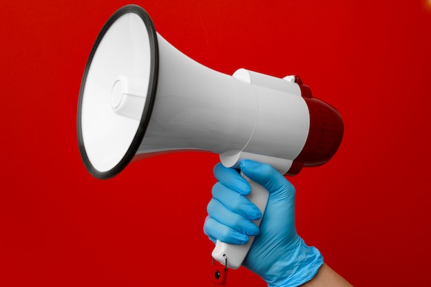 Human hand in medical glove holding electronic megaphone on red