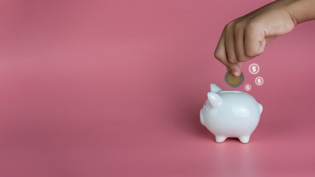 A human hand put a coin in a piggy bank on a pink background Savings and investment concepts