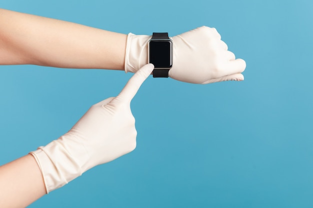 Human hand in surgical gloves holding and showing wirst smart watch and pointing at empty screen.