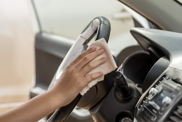 A human hand wipes the steering wheel in a car with a rag. Wash a dirty steering wheel with a cleaner.