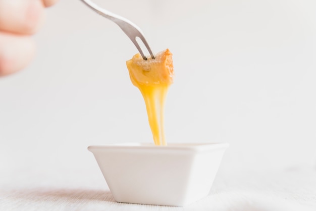 Human hand with bread in cheese fondue on pick