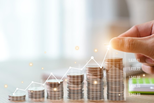 Human hands holding coins and piles of coins with calculator investment prospectus on desk and graph shows the success and growth of the investment