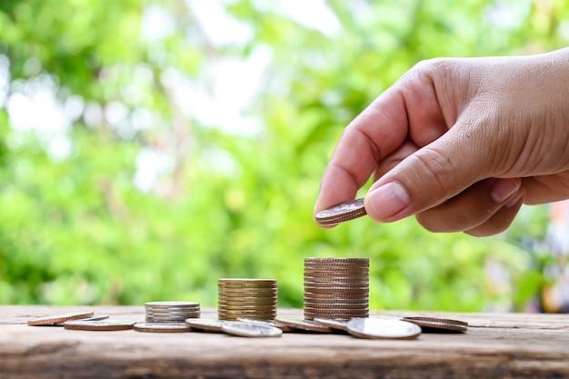 Human hands holding coins and piles of coins on wooden floor financial and investment ideas.