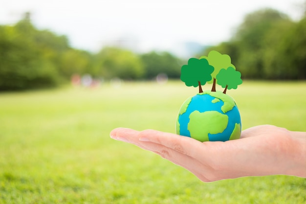 Human hands holding plant trees on the globe, planet or earth over blurred green garden nature background. Ecology concept.