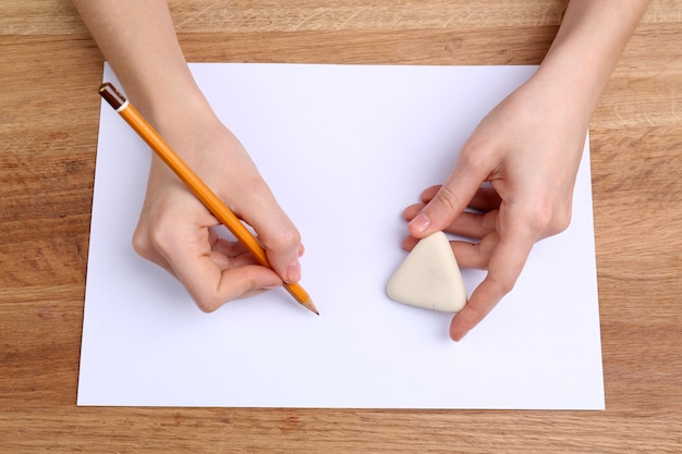 Human hands with pencil writing on paper and erase rubber on wooden table