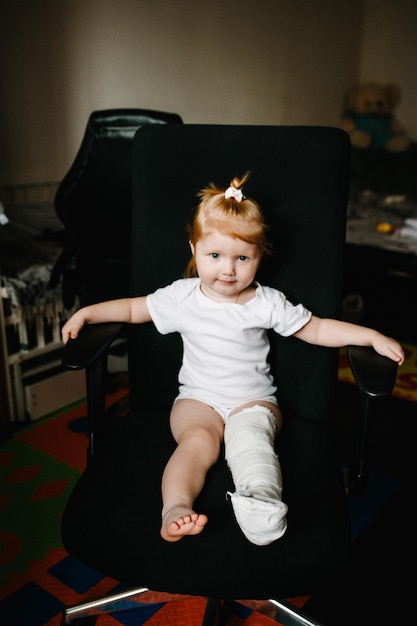 Human healthcare and medicine concept child with bandage on leg heel fracture or broken foot bone Little girl injured sitting on chair at home Close up