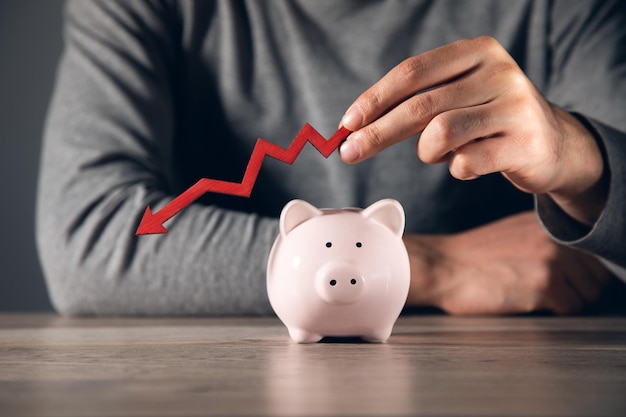 Human Holding Red Arrow In Front Of Pink Piggybank