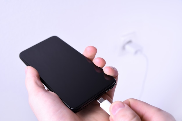 A human ,man hand puts charge the battery mobile smart phone, cellphone ,mobile on the white  with a socket in the frame.