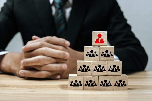 Human resource. human icon on wooden cube block on top pyramid stack with business man in background, creative, business management, team leader, business strategy, human resource management concept