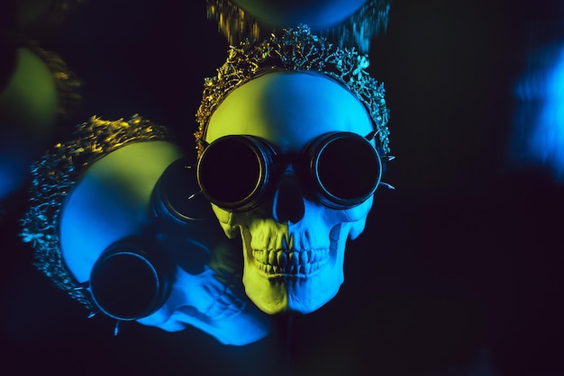 Human skull in a crown and steampunk glasses with colored yellow blue neon light