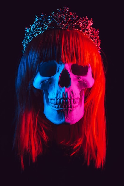 Human skull of a woman in a wig with red hair in a crown with colored pink and blue light