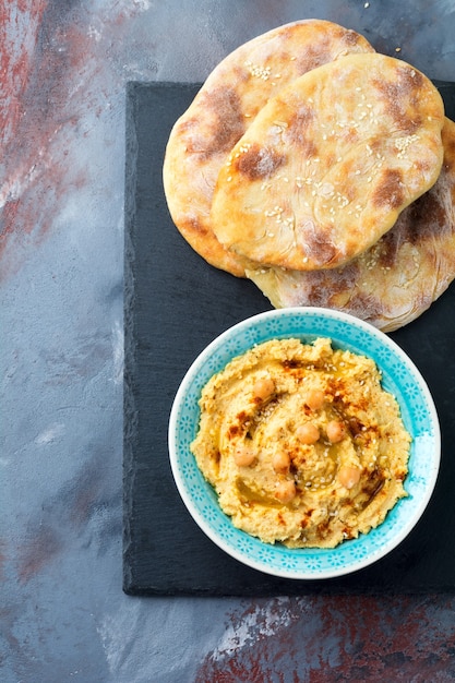 Hummus, chickpeas, with spices and pita, flat cake in a plate on a background of gray stone.