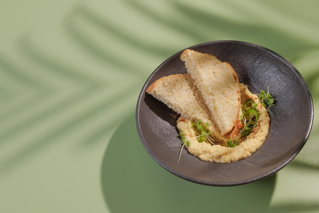 Hummus on a dark plate on a green background with a shadow from a palm tree top view