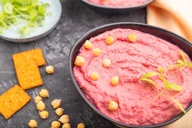 Hummus with beet and microgreen basil sprouts in ceramic bowl on a black concrete background Side view selective focus