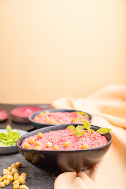 Hummus with beet and microgreen basil sprouts in ceramic bowl on a black and oarange background. 