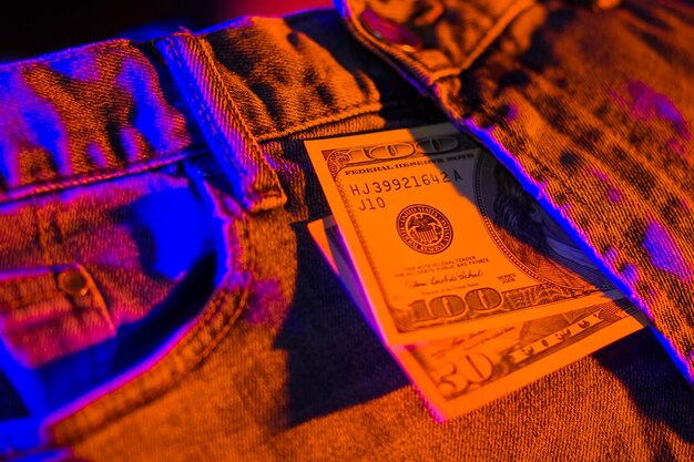 Hundred dollar bill in pocket of blue jeans toned Dollars in neon light