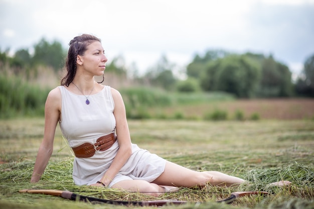 A Hungarian woman in linen dress sitting in the field with a bow