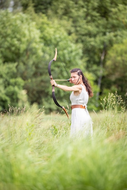 A Hungarian woman in a linen dress standing with a bow in the tall grass