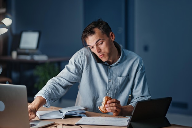 Hungry businessman snacking on a hamburger while working at night