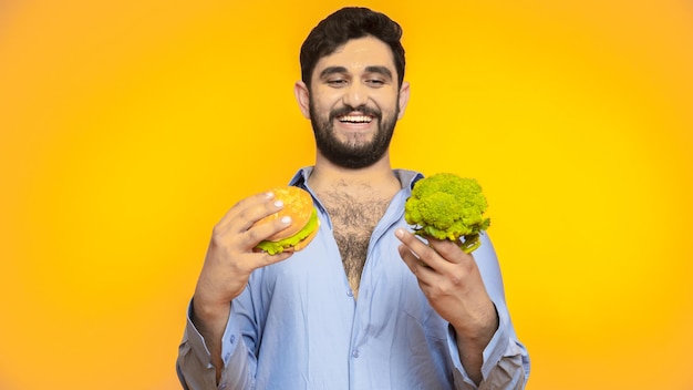 Hungry handsome man holds a hamburger in his hand on yellow background