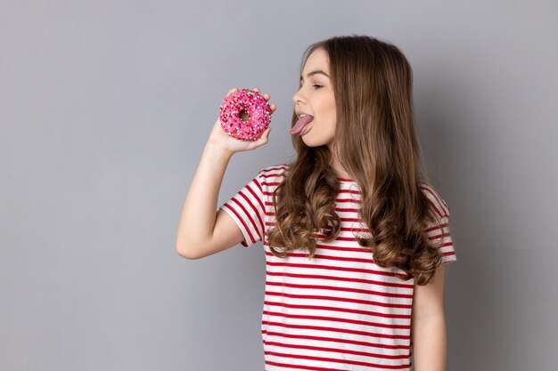 Hungry little girl licking doughnut and showing tongue out sweet sugary confectionary