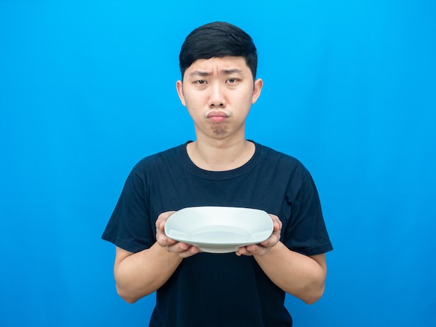 Hungry man holding empty dish gesture want food blue background