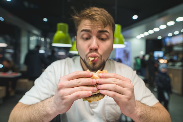 Hungry man with a beard greedily eats a burger. funny man looking at a sandwich. Focus on the burger