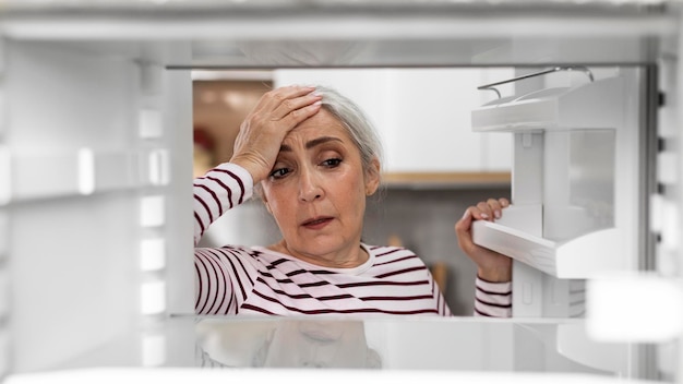 Hungry Senior Woman Looking Inside Of Fridge With No Food