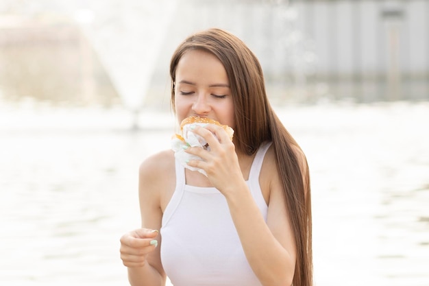 Hungry teenager girl eats hamburger or sandwich at summer picnic lifestyle street food concept