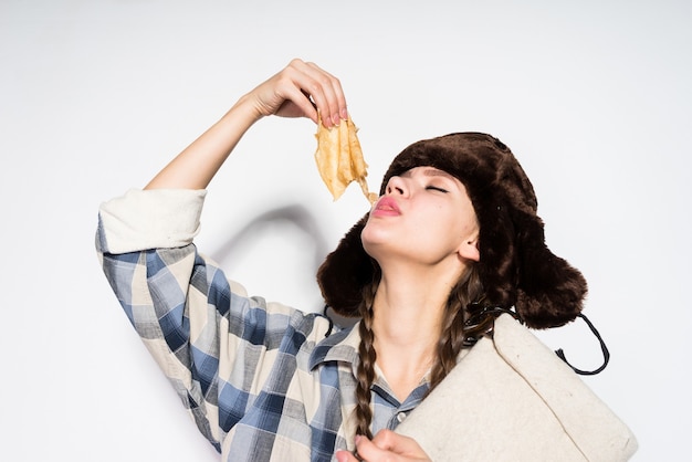 Hungry young Russian girl with fur hat eating hot delicious pancakes, celebrating Shrove Tuesday