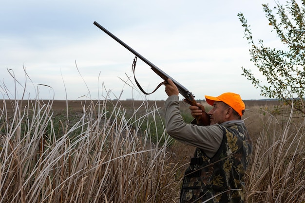 Hunter aiming with rifle while standing against sky in the reeds