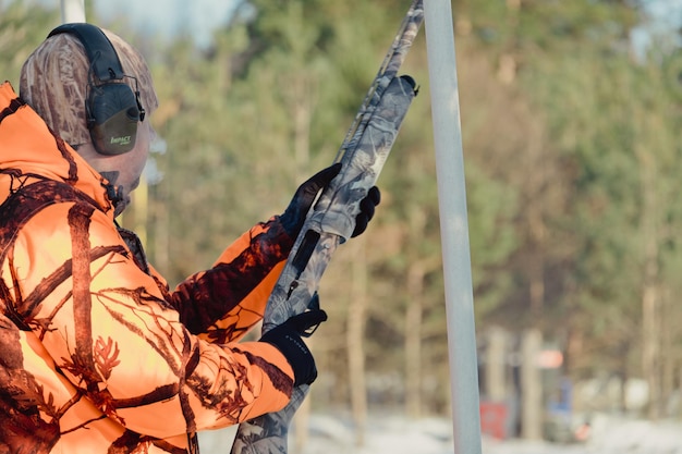 Hunter in camouflage with rifle in winter forest. Hunt concept. Man securing a reserve, on a snowy day. Hunter takes aim from a gun in the snowy forest