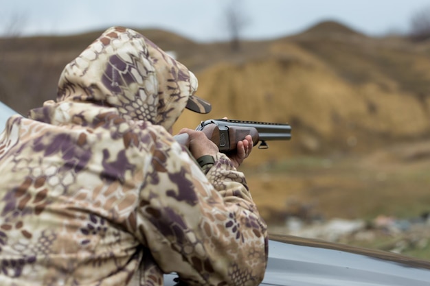 Hunter man in camouflage with a gun during the hunt in search of wild birds or game.