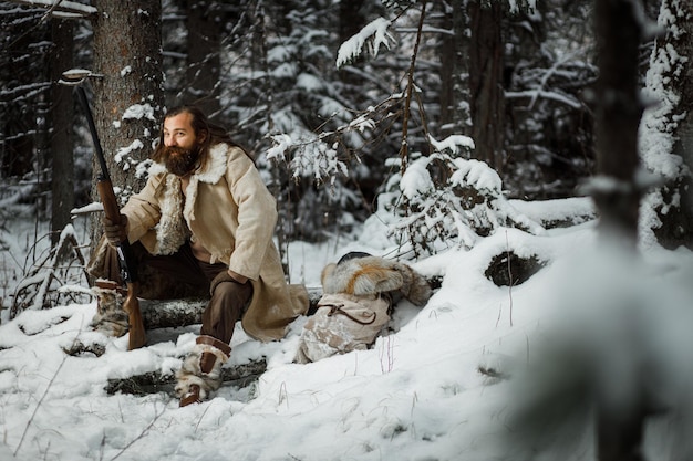 Hunter man in winter warm vintage clothes with gun in winter forest