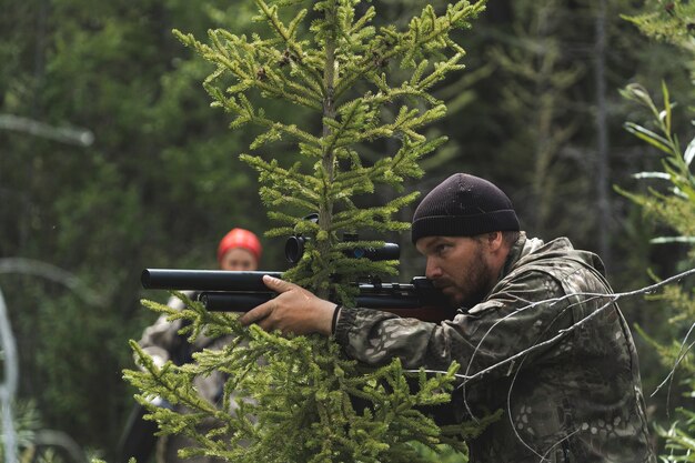 The hunter sits in an ambush with a carbine in his hands. The guy is preparing to shoot a sniper rifle